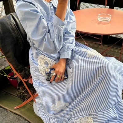 Vestido azul às riscas com bordados florais, mulher sentada, mesa e cadeira laranja