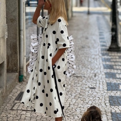 Mulher com vestido branco de bolinhas pretas e sandálias vermelhas a passear com cão em calçada de pedras portuguesas.