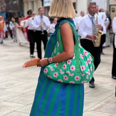Mulher de vestido às riscas e mala floral verde com banda ao fundo