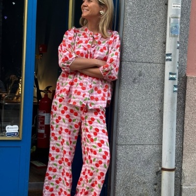 Pijama feminino com padrão de cerejas vermelhas e folhas verdes, camisa e calças largas, em fundo rosa quadriculado