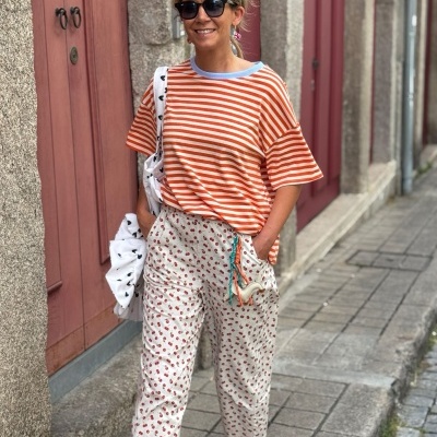 mulher num passeio urbano vestindo t-shirt riscada laranja e branca, calças com padrão floral, óculos escuros e faixa de cabelo verde