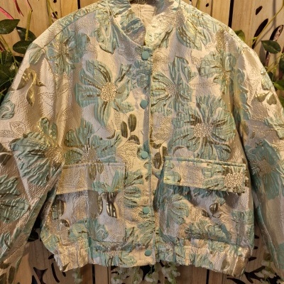 Casaco floral texturado em verde água e bege com botões e bolsos, pendurado em cabide