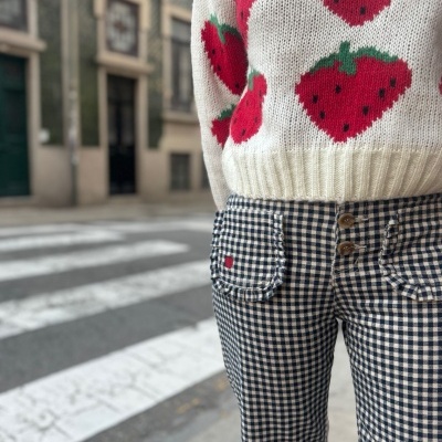 Pessoa a usar calças xadrez preto e branco e camisola de malha branca com morangos, numa rua urbana.