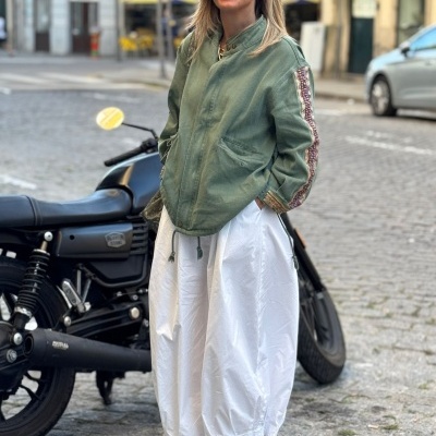 Mulher com casaco verde, vestido branco e sapatilhas, motos em rua urbana