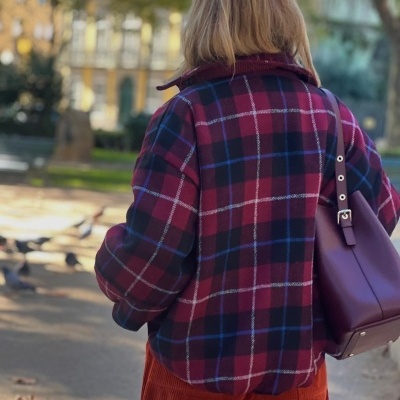 Casaco xadrez vermelho, preto e azul visto de costas com mala bordeaux ao ombro