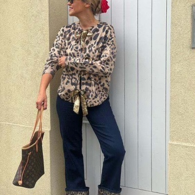 Mulher com blusa animal print, calças azuis, sapatos vermelhos e saco castanho junto a uma porta branca