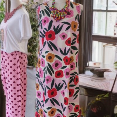 Vestido floral rosa e conjunto branco com calças rosa de bolinhas em manequins, numa sala com decoração floral e janelas