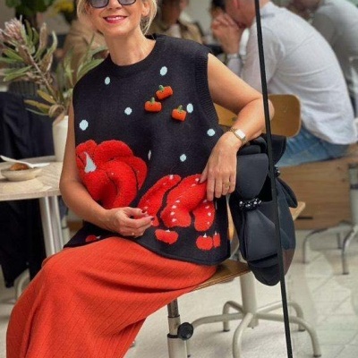 Mulher com colete preto florido vermelho e saia laranja sentada em cadeira