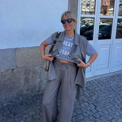 Mulher com roupa cinzenta, t-shirt com texto, óculos escuros numa rua de pedra