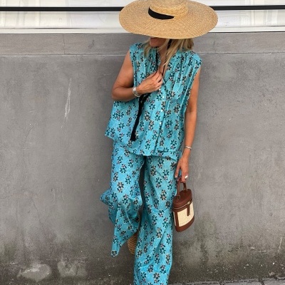 Mulher vestindo conjunto azul com padrão floral, chapéu de palha largo e bolsa castanha em ambiente urbano