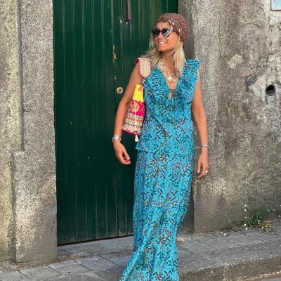 Mulher de vestido azul floral com chapéu e óculos escuros junto a porta verde