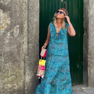 Mulher com vestuário azul floral, acessórios variados, em porta verde antiga