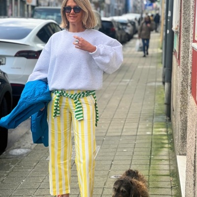 Mulher com roupa casual e cão castanho numa rua urbana pavimentada