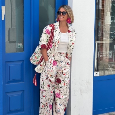 Mulher com conjunto estampado floral e acessórios coloridos junto a porta azul