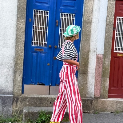 Pessoa com roupa riscada e chapéu bucket a caminhar em frente a portas coloridas.