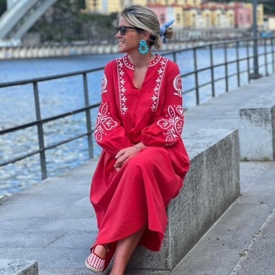 Mulher com vestido vermelho bordado sentada junto a um rio