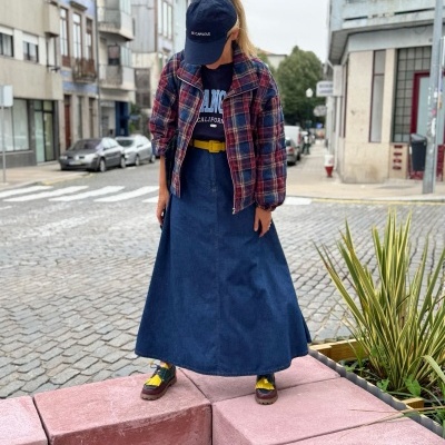 Mulher com vestido azul escuro e camisa xadrez a olhar para baixo na rua