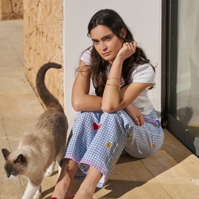 Mulher sentada com calças xadrez azul claro e tênis vermelhos, gato cinzento ao lado