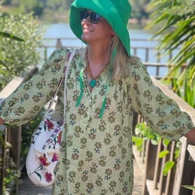 Mulher com vestido floral verde, chapéu verde e óculos escuros em ponte de madeira com vegetação