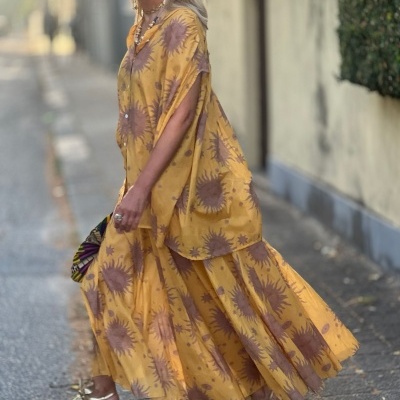 Vestido amarelo longo com estampa de girassóis em rua com calçada e parede