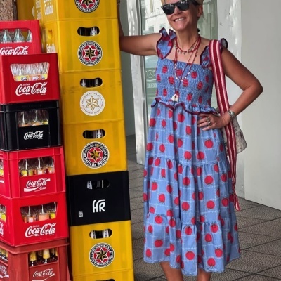 Caixas empilhadas de bebidas ao lado de mulher com vestido azul e chapéu de palha