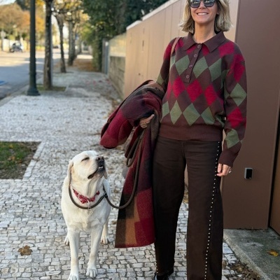 Mulher com camisola xadrez e calças castanhas a passear cão branco numa calçada de pedra