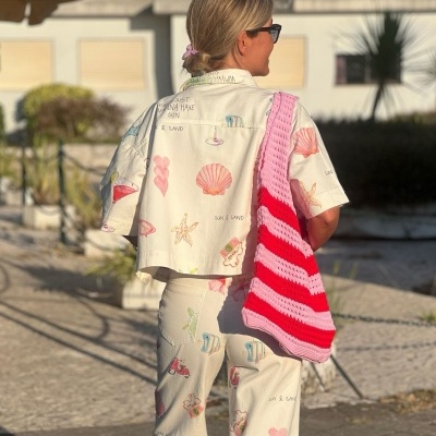 Mulher de costas com conjunto bege estampado e bolsa rosa e branca ao ar livre
