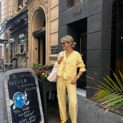 Mulher com roupa amarela e sapatos amarelos junto a placa de happy hour em rua urbana