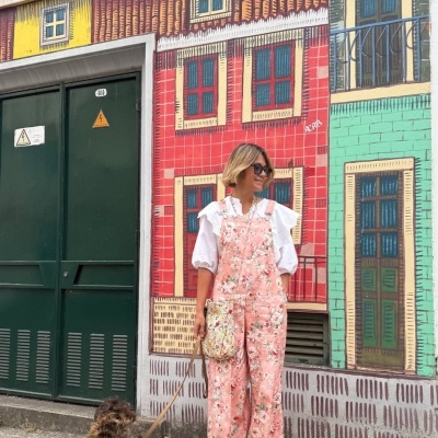 Mulher com macacão rosa floral, blusa branca, óculos escuros e cachorro ao lado