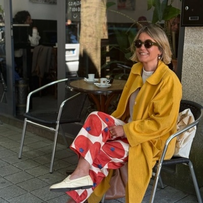 Mulher com casaco amarelo e calças coloridas sentada numa esplanada de café