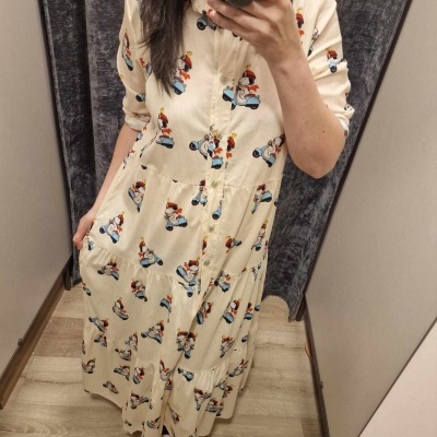 Vestido comprido bege com padrão de personagens em scooters azuis numa cabina de prova