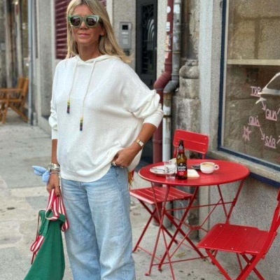 Mulher casual na rua com camisola branca, calças de ganga e mala verde junto a mesa vermelha