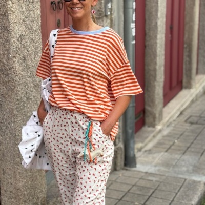 Mulher com t-shirt riscada laranja e branca e calças floridas brancas numa rua urbana