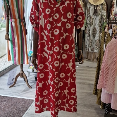 Vestido longo vermelho e branco com padrão floral em manequim de madeira na loja.