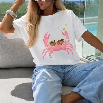 Mulher de t-shirt branca com caranguejo estampado, chapéu de palha e óculos de sol