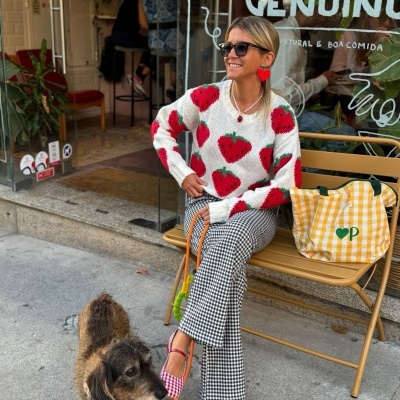 Mulher com camisola com padrão de morangos e calças xadrez sentada num banco amarelo com cão ao lado