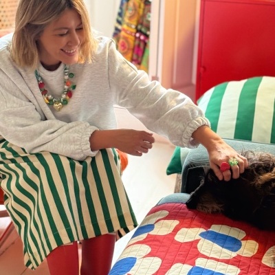Mulher a fazer festas a cão preto num sofá com colcha vermelha com padrão floral.