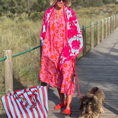 Mulher com vestido e manta coloridos e bolsa às riscas numa passadeira de madeira com cão ao lado