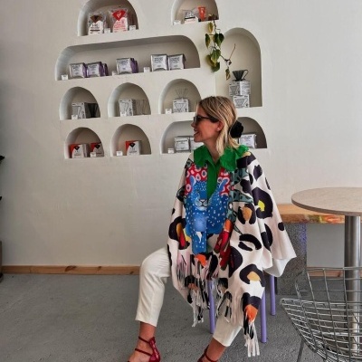 Pessoa com vestuário colorido sentada junto a parede com prateleiras embutidas contendo pacotes brancos e cinzentos