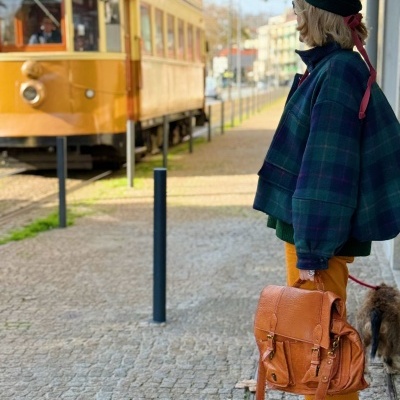 Pessoa com casaco azul e mochila castanha junto a elétrico amarelo