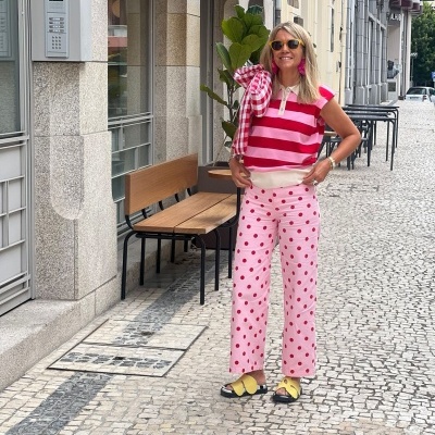 Mulher com roupa colorida e padrão de riscas e bolinhas numa rua urbana com calçada de pedra