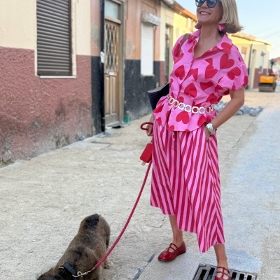 Mulher com roupa rosa e vermelha a passear cão castanho numa rua