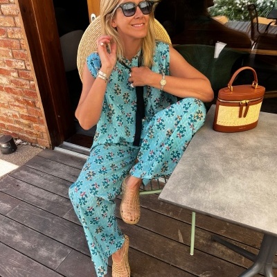 Macacão azul com padrão floral, bolsa bege, mulher sentada ao ar livre