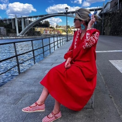 Mulher sentada à beira do rio com vestido vermelho estampado e sapatos xadrez