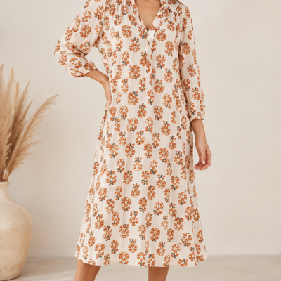 Vestido midi bege com padrão floral laranja e verde, vestido com mangas três quartos e sandálias castanhas.