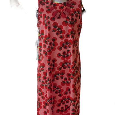 Vestido cor-de-rosa com estampa de tomates e folhas verdes num manequim beige com base de madeira.