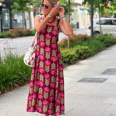 Vestido comprido de padrão floral rosa e verde, sapatos rosas, bolsa branca com flores, senhora com óculos de sol.