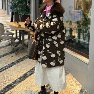 Mulher com casaco felpudo castanho e branco junto a janela