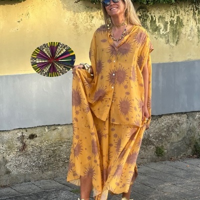 Mulher com conjunto amarelo floral, sandálias douradas e leque colorido em ambiente exterior