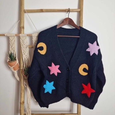 Cardigã preto com estrelas e luas coloridas pendurado num cabide em estrutura de bambu
